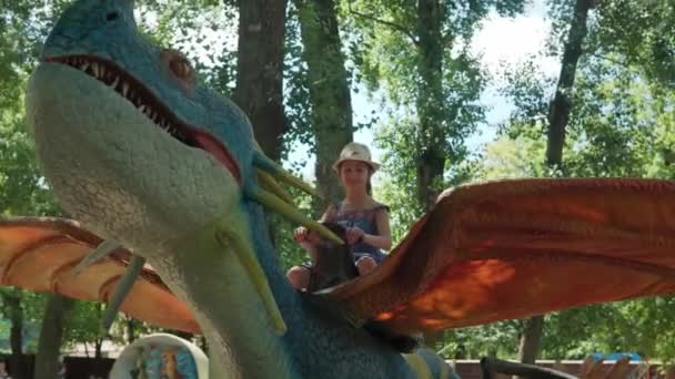 2021.08.12 - Kiev, Ucrania: Niña sentada en un dinosaurio motorizado Predator Dragon Mockup en el Parque Forestal de Atracciones. Exposición de Modelos en Movimiento Animales del Período Prehistórico Jurásico en Dinopark — Vídeo de stock