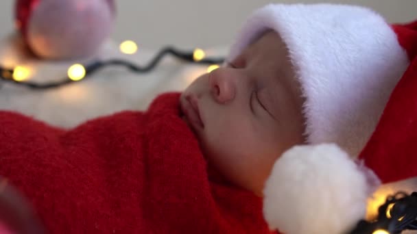 2013 년 7 월 17 일에 확인 함 . Close Up Portrait First Days of Life Newborn Cute Funny Sleeping Baby In Santa Hat Wrapped In Red Diaper At White Garland Background. 메리 크리스마스, 해피 뉴 이어, 유아, 어린 시절, 겨울 컨셉 — 비디오
