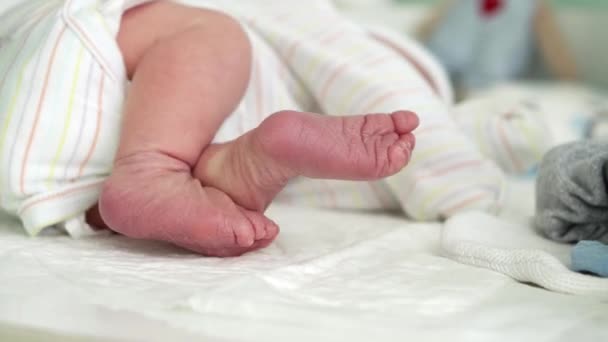 Kleine schattige pasgeboren baby 's Bare Feet en tenen eerste dagen van het leven op witte achtergrond. Close-up van kleine benen droge huid van baby zuigeling. Mam verschoont luiers op de aankleedtafel.Kindertijd, Moederschap Concept. — Stockvideo