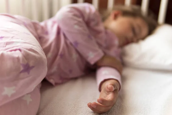 Lindo y alegre niñito de 3-4 años que duerme dulcemente en una cuna blanca durante el descanso del almuerzo en pijama rosa con almohada en casa. Infancia, ocio, comodidad, medicina, concepto de salud — Foto de Stock