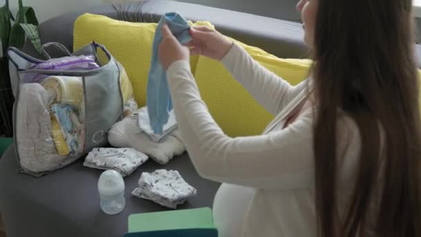 Carino incinta donna scrittura lista imballaggio per maternità ospedale notebook prepara borsa. Giovane Ledy in gravidanza Divertiti a trascorrere del tempo sul divano grigio giallo a casa. Maternità, Medicina Concetto sanitario — Video Stock