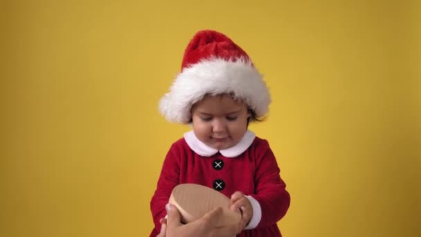 Happy Cheerful Chubby Toddler Baby Girl in Santa Suit Looking On Camera At Yellow Background Діти грають різдвяну сцену, святкуючи день народження. Хлопцю дарують подарунок на Новий рік. — стокове відео