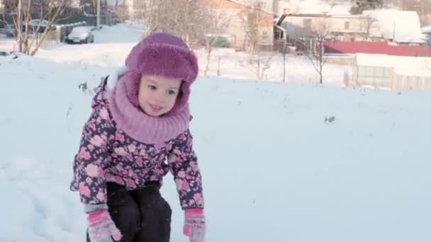 Zima, wakacje, gry, koncepcje rodzinne - zbliżenie autentyczne małe przedszkole moll 3-4 lat dziewczyna w fioletowym na pokryte śniegiem łąki skacze i spada łupy na śniegu. dziecko biegnie po śnieżnej okolicy — Wideo stockowe