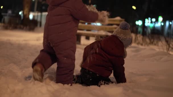 Inverno, vacanza, giochi, concetti di famiglia - piano intermedio di autentici felici fratellini dell'infanzia I bambini si divertono nel parco serale, scolpiendo palle di neve cadono sulla neve con il freddo gelido — Video Stock