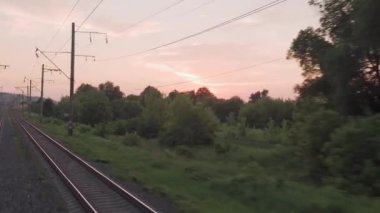 Pencereden yüksek hızlı tren manzarası güzel doğa manzarası vahşi arazi ve orman rayları yaz arkaplanında akşam günbatımında tren rayları. Ulaşım, seyahat, demiryolu, iletişim konsepti