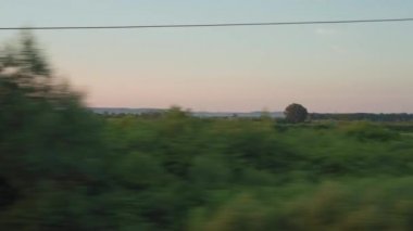 Yüksek hızlı trenin penceresinden manzarası güzel doğa manzarası vahşi arazi ve orman akşam bulutlu gökyüzü günbatımı yaz arkaplanında. Ulaşım, seyahat, demiryolu, iletişim konsepti