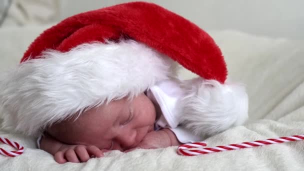 メリークリスマスと幸せな新年、幼児、子供時代、休日のコンセプト-人生の終わりの最初の日サンタクラスの赤い帽子の赤い帽子の上に白い背景にキャンディー杖で嘘をつく — ストック動画