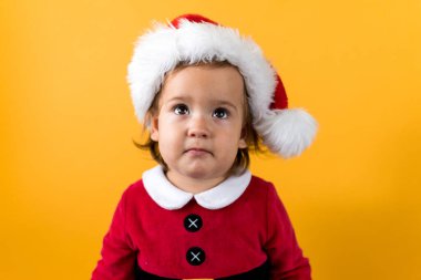 Gülümseyen Portre Şirin, neşeli, tombul kız Noel Baba Şapkalı Sarı Arkaplan 'la ilgileniyor. Doğum gününü kutlayan çocuk Noel Sahnesi oynuyor. Çocuk Yeni Yıl Fotokopi Alanını Eğlenerek Geçiriyor