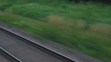 Pencereden yüksek hızlı tren manzarası güzel doğa manzarası vahşi arazi ve orman rayları yaz arkaplanında akşam günbatımında tren rayları. Ulaşım, seyahat, demiryolu, iletişim konsepti
