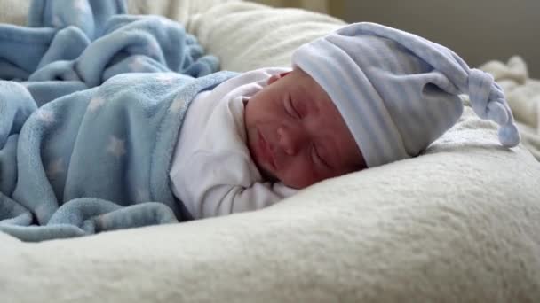 特写新生儿脸谱早睡早起睡在忧郁的蓝白背景上。《帽子上生命的开始时刻的孩子》。婴儿、分娩、分娩的第一时间、开始概念 — 图库视频影像
