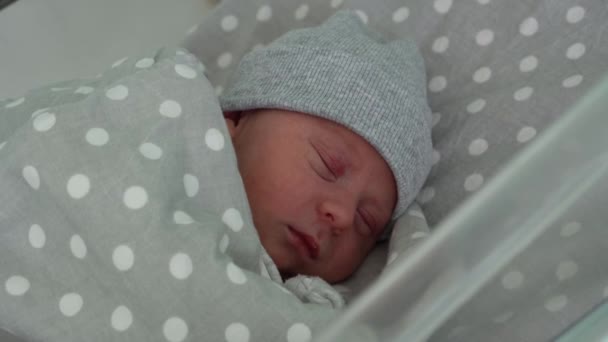 新生児赤ちゃんかわいい顔の肖像画灰色の背景に医療用ガラスベッドで寝る初期の日.帽子の上の生活の開始時に子供。幼児、出産、誕生の最初の瞬間、概念の始まり — ストック動画