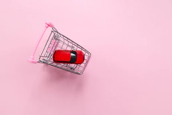 Pastel pembe arka planda alışveriş arabasında kırmızı oyuncak araba, üst manzara, fotokopi alanı. İnternetten araba alma fikri, Sevgililer Günü hediyesi, kadın alışverişi, kiralama hizmetleri. Yatay.