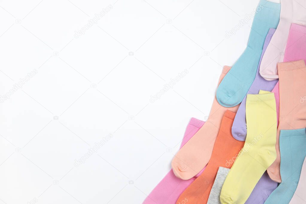 Multicolored children's socks without pattern, laid out in corner of frame, on white background with copy space, flatly, minimal style. Concept children's clothing, housekeeping.