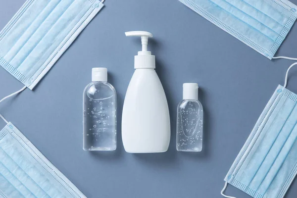 Medical protective, blue face masks, sanitizer gel, liquid hand soap on gray background, close-up, flatly, minimal. Hygiene concept, protective equipment, prevention of spread of viral infections.