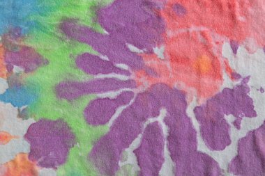 Pastel kravat boyası, pamuk bir tişörtte el yapımı desen. Yakın çekim, üst görüş. DIY konsepti, el sanatları, orijinal günlük kıyafetler, kumaş boyama teknikleri. Düz, yatay. Soyut arkaplan.