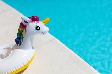 Şişirilebilir pembe gökkuşağı tek boynuzlu atı, güneşli bir günde yüzme havuzunun yanında kokteyl standı, fotokopi odası. Yaz tatili, eğlence, su, hava, güneş banyosu, sağlık. Yan görüş. Yatay.