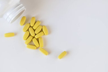 Beyaz arka planda hap kavanozunun yanında duran sarı uzun vitaminler, makro, yakın plan, kopyalama alanı. Besin takviyeleri konsepti, sağlık, vitaminler, 2021 'in moda rengi, aydınlatıcı. Yatay.