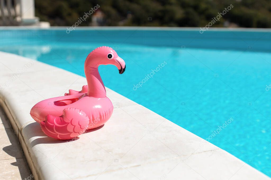 Inflatable pink mini flamingo, cocktail stand near swimming pool on bright sunny day, copy space. Concept of summer vacation, entertainment, water, air, sunbathing, health. Side view. Horizontal.