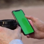 Aus nächster Nähe, die Hände eines kaukasischen Mannes mit Tasse Kaffee und Smartphone mit grünem Bildschirm, Chroma-Taste, Scrollen, Touchscreen. Seitenansicht. Attrappe auf. Technologiekonzept, Online-Shopping, Kommunikation.