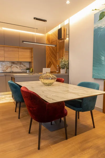 Stylish modern kitchen interior, studio. Large table with velvet chairs. Zone in living room, dining room, designer wood veneer panel on wall. Concept minimal fashionable interior, natural materials.