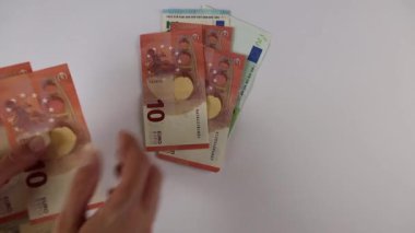 Tanımlanamayan beyaz kadın avroluk banknotları sayıyor. Kağıt para ve paraları beyaz masaya serer. Sadece eller görünür. Paradan arkaplan. Yukarıdan bak. Finans, para, bütçe kavramı.