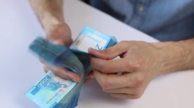 Tanınmayan beyaz bir adam Rus rublesi sayıyor, 2000 banknot, banknotlar, beyaz bir masanın üzerinde yatıyor. Sadece eller görülebilir. Yan görüş. Finans, para, gelir kavramı.