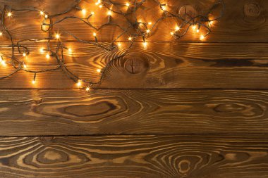 Noel arkaplanı. Kahverengi ahşap tahtalarda parlayan çelenkler, bir tarafta. Boşluğu, düzlüğü, üst görüntüyü kopyala. Tatil, Noel, yeni yıl, parti konsepti, mesaj için yer belirleme. Yatay.