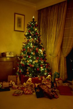 Noel ağacı süslenmiş renkli toplar ve yerde hediye kutuları olan küçük ışıklar..