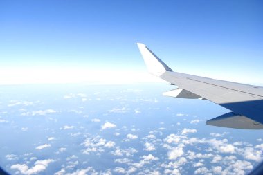 Havada uçuşan uçağın beyaz kanatları ile güzel bir mavi gökyüzü. Uçak penceresinden görüntüle