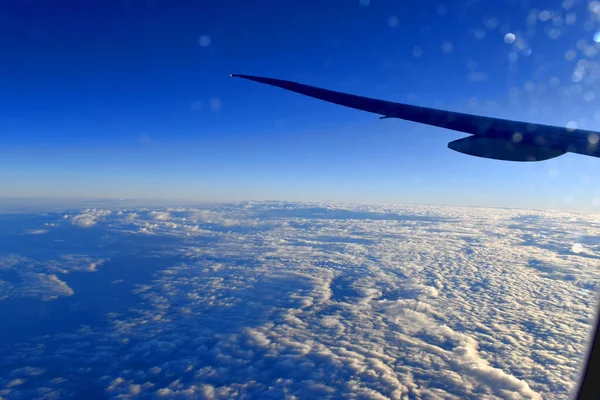 航空機の翼の下に劇的な光と青い空の背景を持つ空の美しい雲 飛行機の窓からの眺め — ストック写真