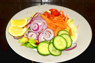 Salata için organik sebzeleri hazırlamak, salatalık, havuç, domates, kırmızı soğan ve arka planda gri tabakta yeşil marul. Sağlıklı yemek ve evde kolay yemek..