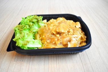 Tayland yemeği, ahşap arka planda plastik tepside siyah soya soslu kızarmış erişte (Pad See Ew). Bangkok, Tayland 'da otel karantinasındaki yolculara hazır yemek.