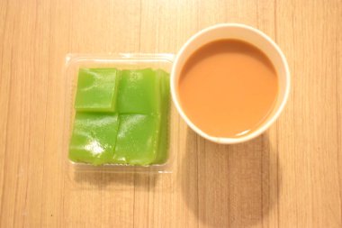 Tahta arka planda Tayland tatlısı buharlı Pandan Katman Keki (Kanom Chan) ile bir fincan sıcak sütlü çay eşliğinde görüntülenmiştir..