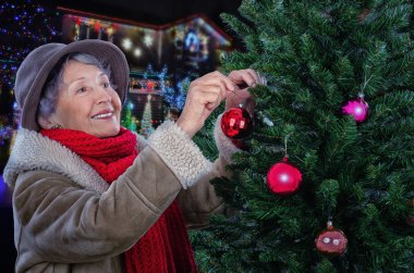 Senior woman in sheepskin jacket decorating Christmas tree clipart