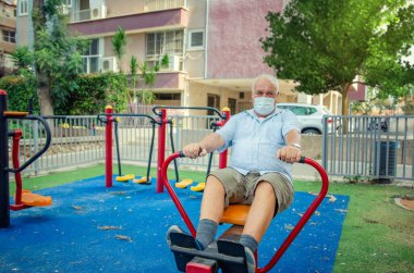 Yüz maskeli yaşlı vatandaş Coronavirus 'a rağmen her gün kürek çekme makinesinde çalışıyor..