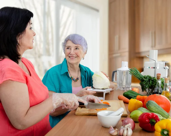 A compassionate neighbor or rented actress and lonely old woman prepare a vegetable dish together. The elderly lady is very pleased.