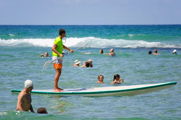 Lifeguard stand up paddling among swimmers — Stock Photo, Image