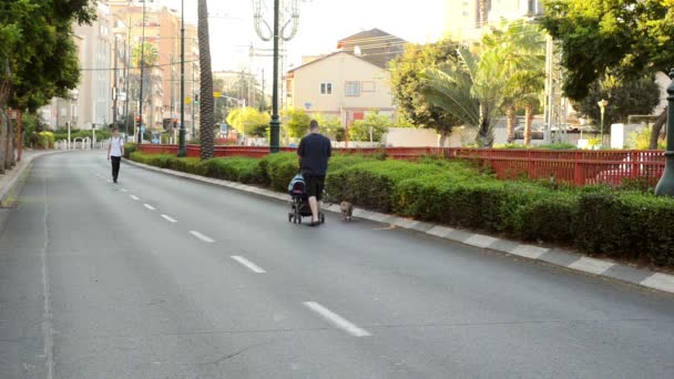 Парень катает коляску по пустой городской дороге — стоковое видео