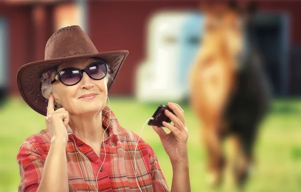 Senior cowgirl listening music on smartphone — Stock Photo, Image