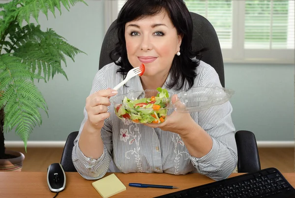 Mulher de cabelos pretos está comendo salada para almoço de escritório — Fotografia de Stock