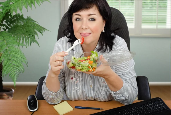 Siyah saçlı kadın ofis öğle yemeği için salata yiyor Stok Resim