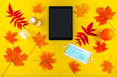 Maskeli tablet bilgisayar ve sonbahar yapraklı dezenfektan şişesi..