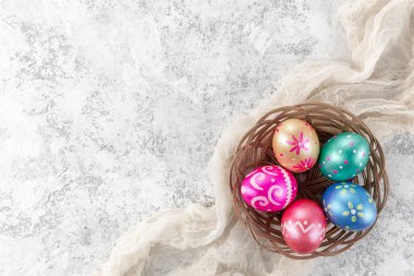 Beş paskalya yumurtası, koyu mavi, yeşil, turuncu, morumsu ve altın renkli, beyaz arka planda sepetle süslenmiş. Metin için alanı kopyala.
