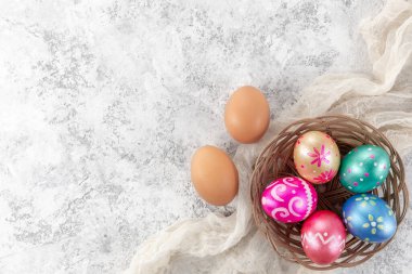 Beş paskalya yumurtası, koyu mavi, yeşil, turuncu, morumsu ve altın renkli, beyaz arka planda sepetle süslenmiş. Metin için alanı kopyala.