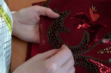 Tahta masa üzerinde boncuklu terzi nakışçısı kırmızı yeleğin kısmi görüntüsü