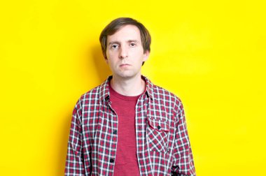 Kırmızı kareli gömlekli yakışıklı sinirli adam sarı arkaplanda fotokopi alanı olan kameraya bakıyor.