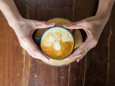 Bir fincan sıcak kahve içecek ahşap masa üzerinde holding kadın eller