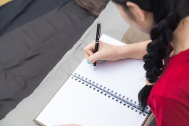 Hoş, sevimli Asyalı genç bir kadın yatağın üzerine kitap yazmış kırmızı gömlekli kadınlar ve kitapçık.