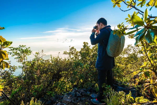 Молодой человек с рюкзаком фотографируется на вершине гор — стоковое фото