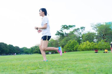 Parkta koşan genç fitness kadını yeşil çimlerde, spor yapan kadınlar.